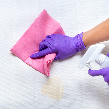 Hands wearing purple gloves attempt to remove stain from mattress